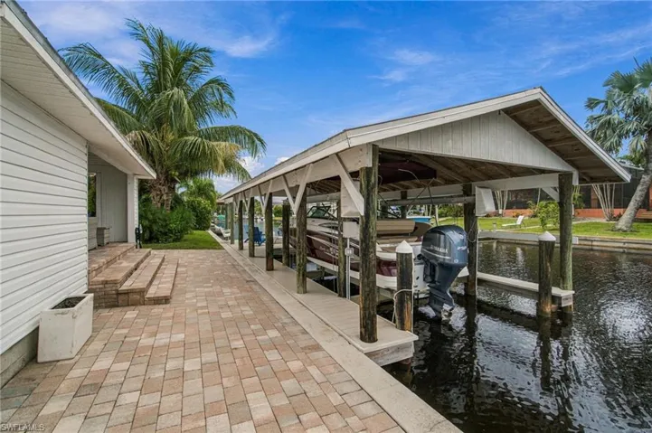 Waterfront property featuring a covered boat dock, paver patio, sloped entry steps, and mature palm trees
