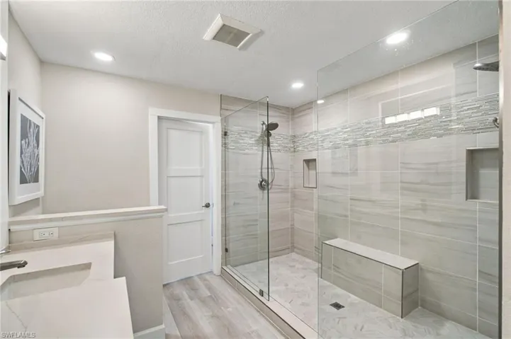 Walk-in shower with clear glass enclosure, light-toned tile flooring, and integrated shower bench