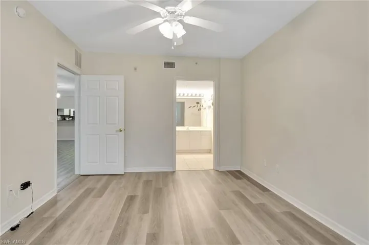 Unfurnished bedroom featuring light wood finished floors, baseboards, ensuite bath, and ceiling fan