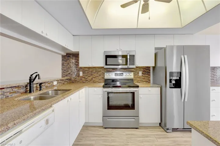 Kitchen with stainless steel appliances, a sink, backsplash, a ceiling fan, and white cabinetry