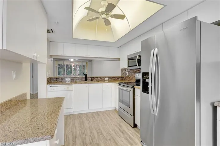 Kitchen with stainless steel appliances, ceiling fan, white cabinetry, a sink, and backsplash