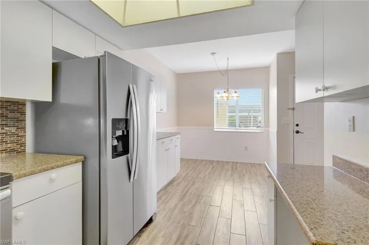Kitchen featuring light wood-style flooring, stainless steel fridge with ice dispenser, a chandelier, and white cabinets