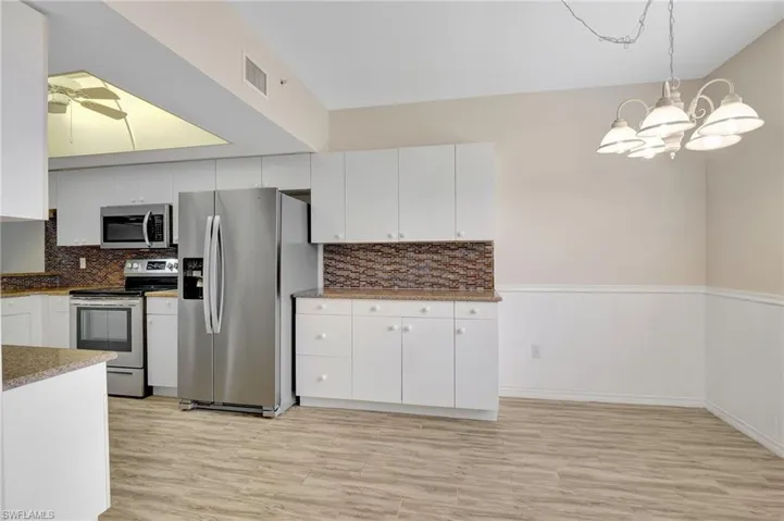 Kitchen with appliances with stainless steel finishes, white cabinets, light wood-type flooring, a chandelier, and a wainscoted wall