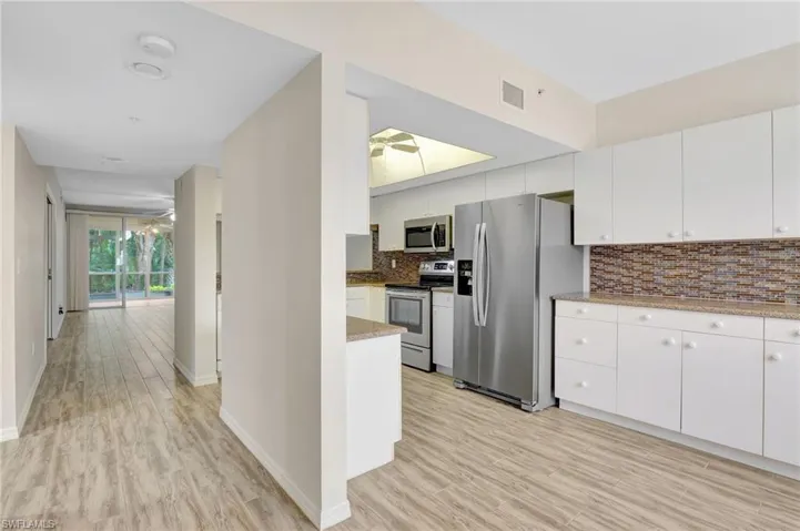 Kitchen with stainless steel appliances, backsplash, white cabinetry, and light wood-type flooring