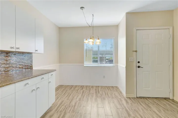 Kitchen with a chandelier, white cabinetry, light wood-style flooring, tasteful backsplash, and baseboards