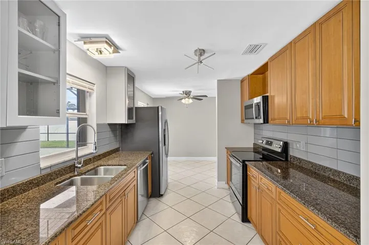 Kitchen featuring appliances with stainless steel finishes, decorative backsplash, a ceiling fan, light tile patterned floors, and glass insert cabinets
