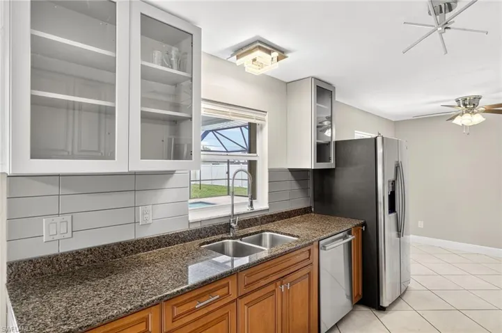 Kitchen with appliances with stainless steel finishes, brown cabinets, ceiling fan, glass insert cabinets, and light tile patterned flooring