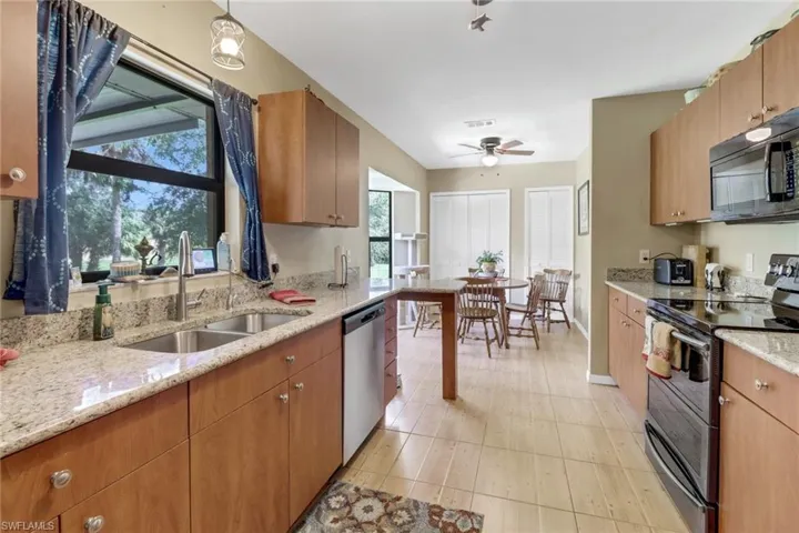 Kitchen featuring sink, stainless steel appliances, decorative light fixtures, light stone countertops, and ceiling fan