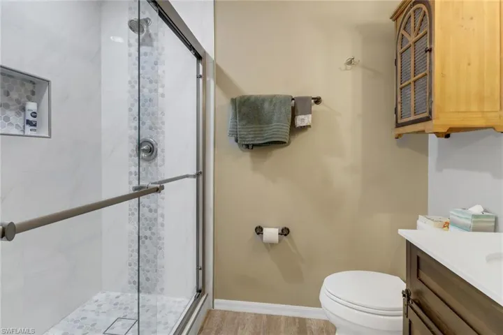 Bathroom featuring wood-type flooring, vanity, toilet, and a shower with door