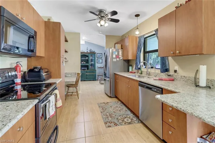 Kitchen with light stone counters, pendant lighting, stainless steel appliances, ceiling fan, and sink