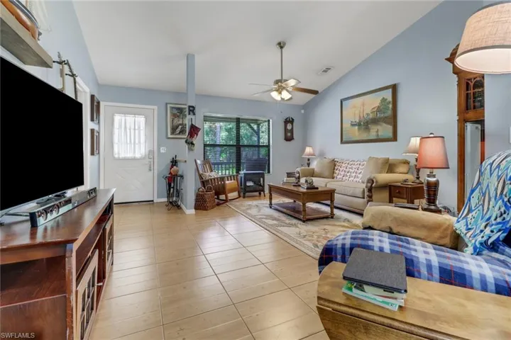Living room featuring vaulted ceiling, ceiling fan, and light tile patterned floors