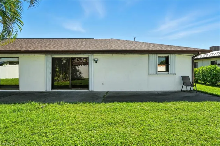 Rear view of house featuring stucco siding, a yard, and a shingled roof