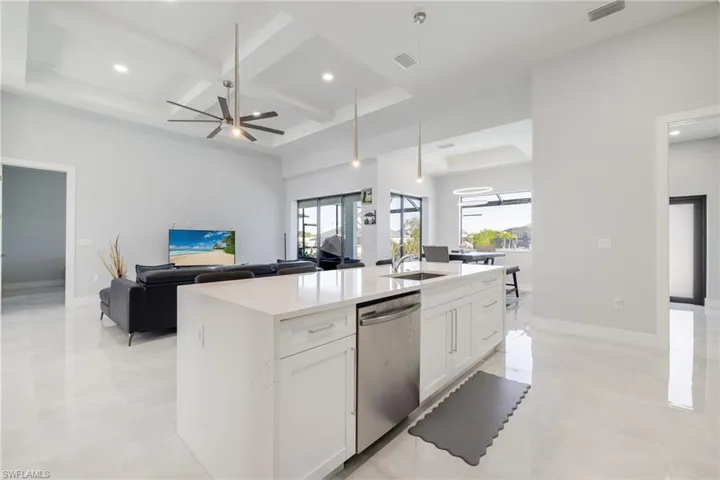 Kitchen with coffered ceiling, open floor plan, white cabinetry, light stone counters, and stainless steel dishwasher