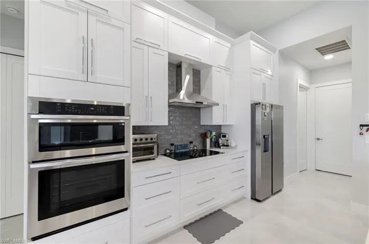 Kitchen featuring appliances with stainless steel finishes, wall chimney exhaust hood, white cabinetry, decorative backsplash, and light stone counters