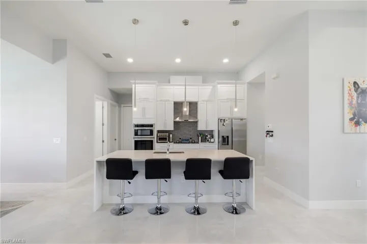 Kitchen featuring a breakfast bar, wall chimney range hood, white cabinetry, appliances with stainless steel finishes, and a center island with sink