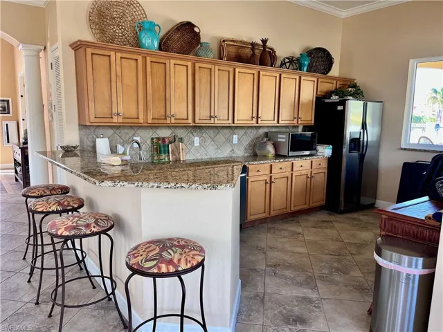 Club house community room kitchen featuring brown cabinets, ornamental molding, a kitchen breakfast bar, light stone counters, and appliances with stainless steel finishes