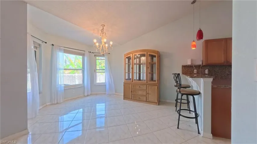 Dining room featuring vaulted ceiling and a chandelier with adjacent breakfast bar