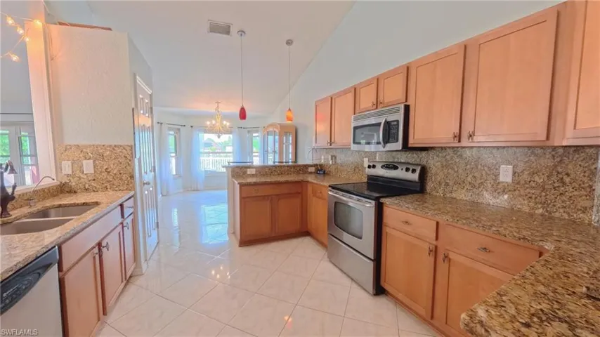 Kitchen showcasing stainless steel appliances, granite countertops with backsplash, a peninsula, and tiled flooring