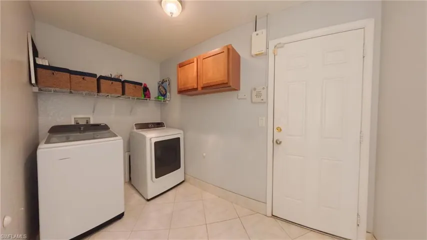 Laundry area featuring patterned tile floors, separate washer and dryer, and cabinet space