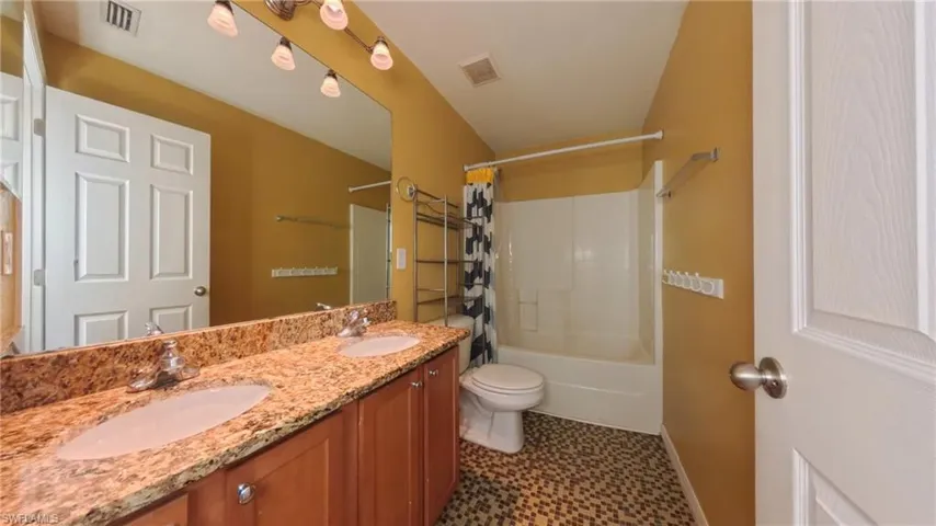 Guest bathroom featuring double vanity, shower / bath combo, and patterned tile flooring