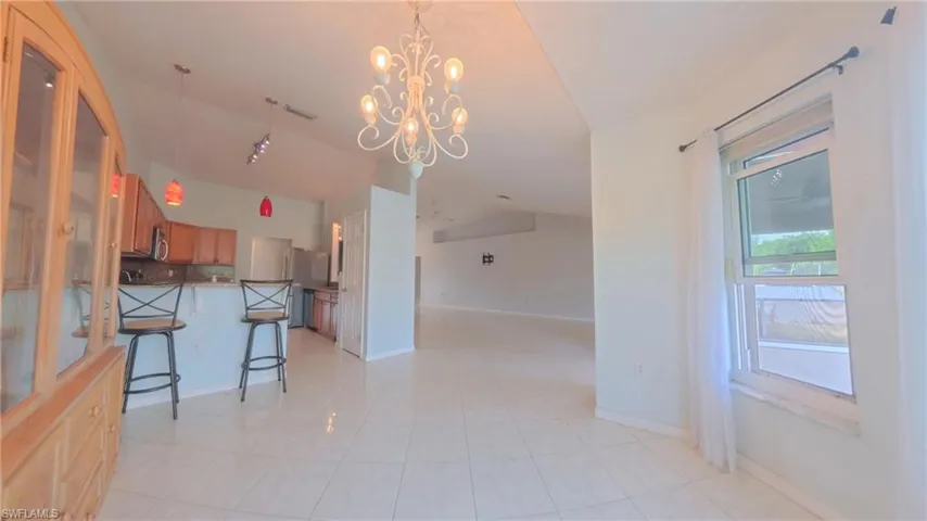 Kitchen area featuring hanging light fixtures, brown cabinetry, chandelier, breakfast bar, and lofted ceiling