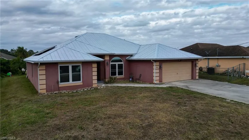Single story home featuring metal roof and solar panels, stucco siding, a front yard, and an attached 2 car garage