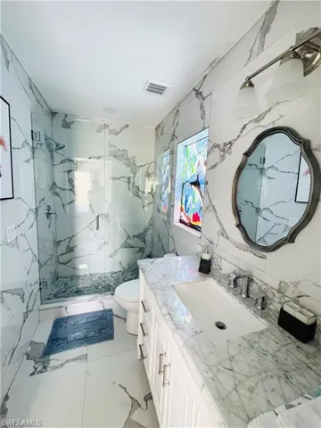 Bathroom with vanity, a marble finish shower, stone wall, tile walls, and light marble finish floors
