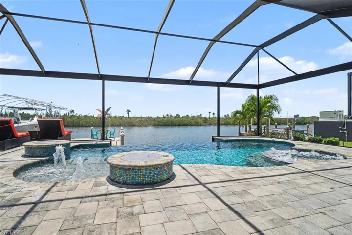 The screened outdoor living area features a pool, a hot tub, and an additional water feature, all surrounded by paver decking