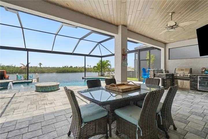 Expansive screened lanai featuring an outdoor dining area, a built-in outdoor kitchen with a grill, a ceiling fan, and a swimming pool with a water view
