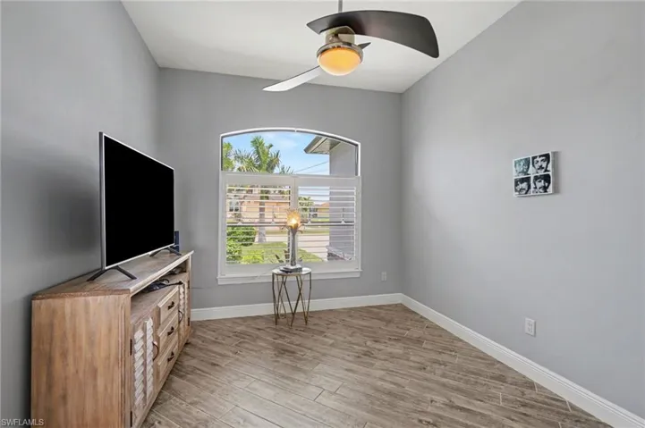 This versatile room features light gray walls, wood-look tile flooring, and a window with white plantation shutters