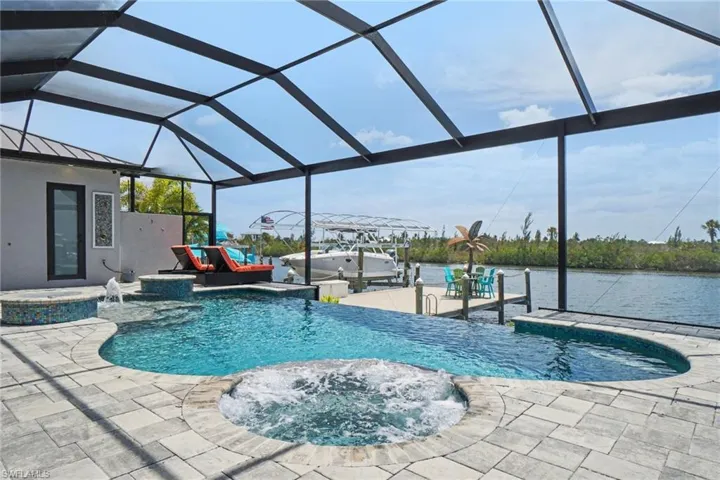 Outdoor living area featuring a screened-in pool and spa, paved patio, and a private dock overlooking the spreader canal