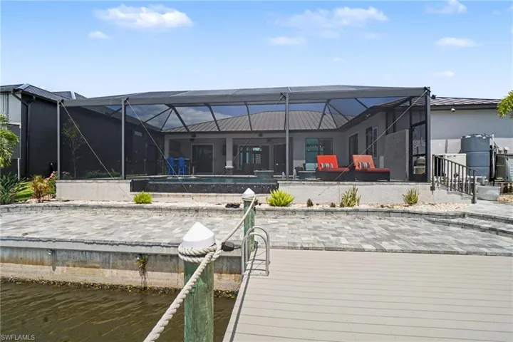 This property features a screened-in pool area, a paved patio with landscaping, and a dock for water access