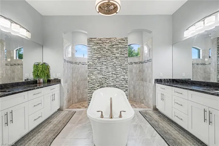 Expansive bathroom featuring a freestanding soaking tub, twin vanity areas with dark countertops and light cabinetry, and separate shower enclosures with tiled walls