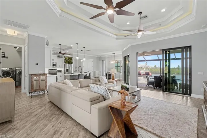 The spacious living area features wood-look tile flooring, tray ceilings with ceiling fans, and sliding glass doors that open to an outdoor living space