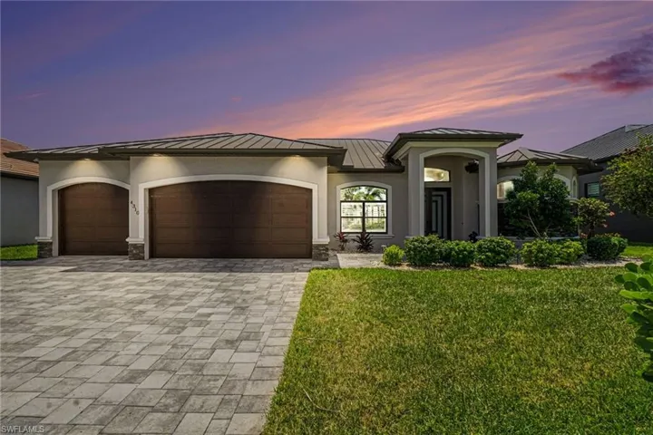 The property features a paver driveway, a two-car garage, and a well-maintained lawn with mature landscaping including palm trees