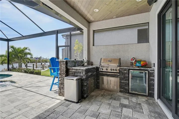 Expansive outdoor living area featuring a built-in kitchen with a grill, refrigerator, and stone finishes