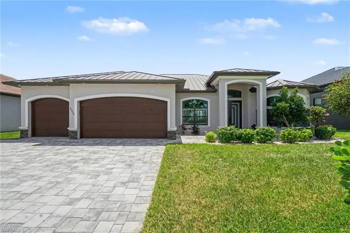 The property features a paver driveway, a two-car garage, and a well-maintained lawn with mature landscaping including palm trees