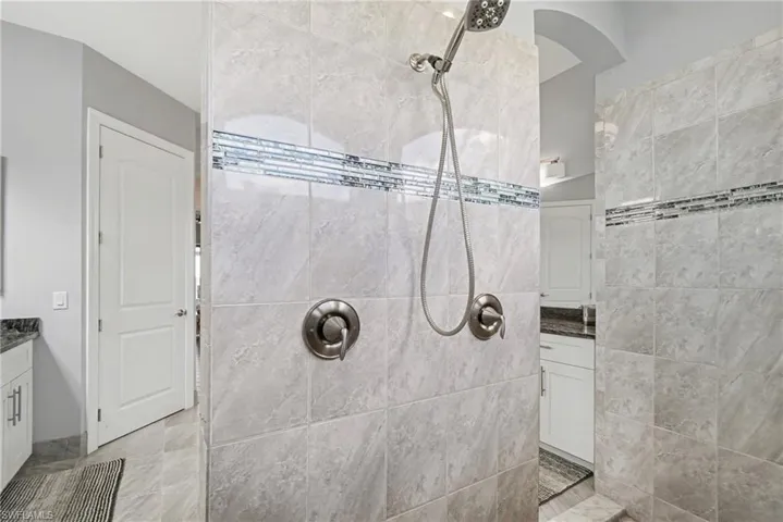 Shower enclosure featuring light grey tiled walls with decorative mosaic accent bands, and a brushed nickel shower head and controls