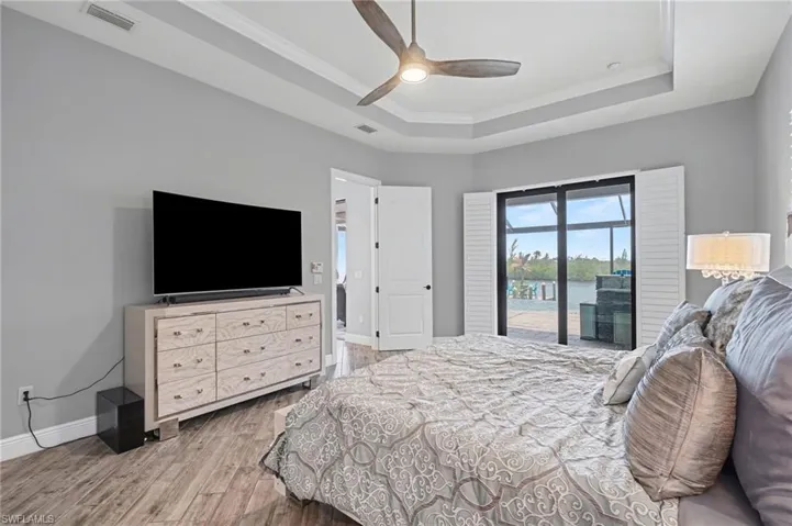 Master Bedroom features a tray ceiling, a ceiling fan, and sliding glass doors that open to a water view with plantation shutters