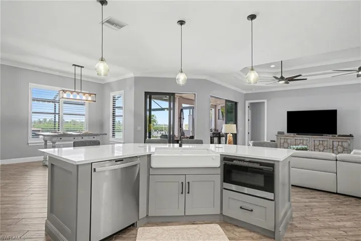 The kitchen features a large island with a white countertop, an integrated farmhouse sink, and a built-in dishwasher and microwave