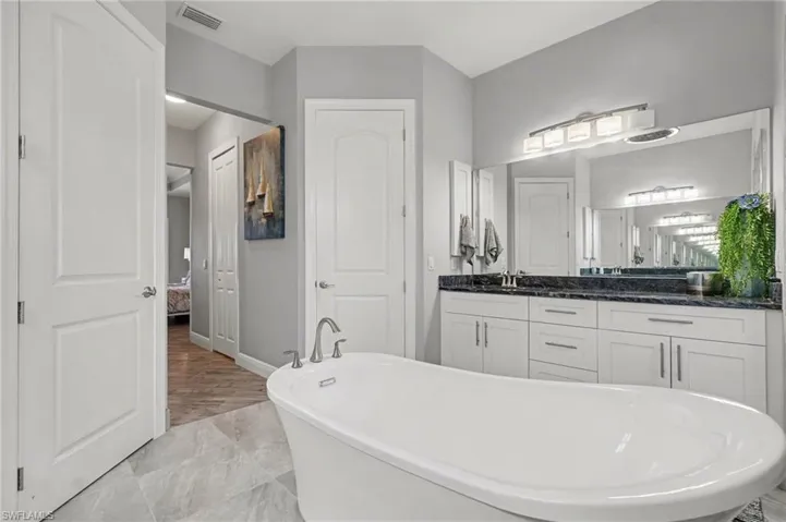 The bathroom features a freestanding bathtub, a vanity with a dark countertop and white cabinetry, a large mirror, and tiled flooring