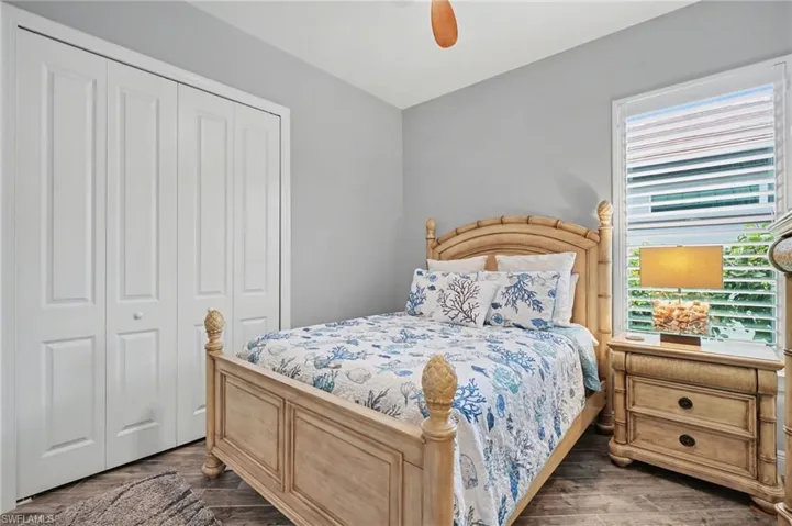 This room features a window with white louvered blinds, textured wood-look tile flooring, and a ceiling fan