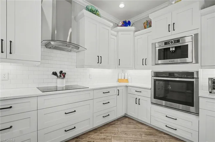 The kitchen features white cabinetry, stainless steel appliances, a white subway tile backsplash, and light-colored countertops