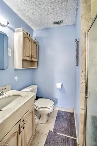 Bathroom with a shower with shower door, tile patterned flooring, vanity, toilet, and a textured ceiling