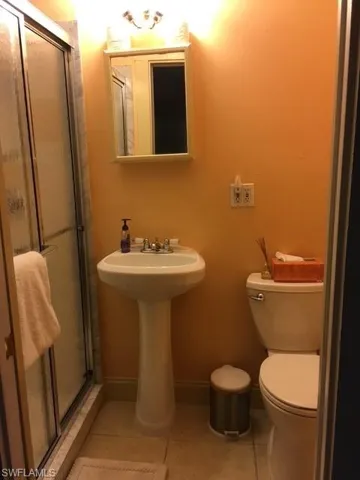 Apt Bathroom with tile patterned floors, toilet, and a shower with door