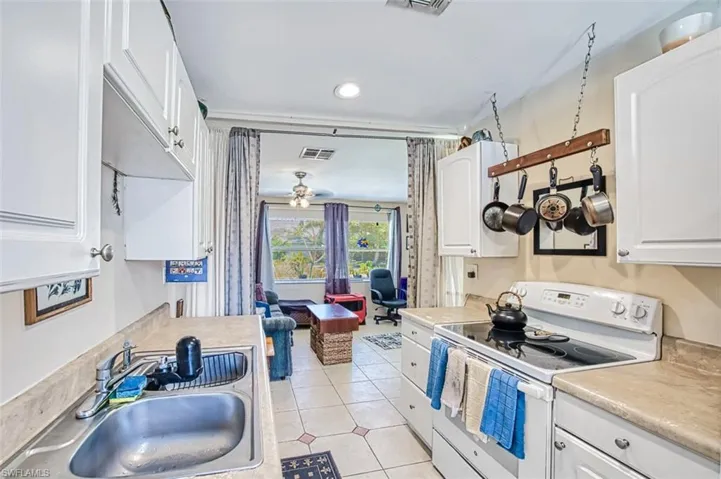 Kitchen with sink, light tile patterned floors, ceiling fan, white cabinetry, and electric range