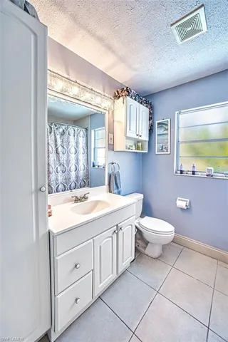 Bathroom featuring vanity, tile patterned flooring, toilet, and a textured ceiling