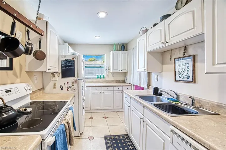 Kitchen with sink, white appliances, white cabinets, and light tile patterned flooring