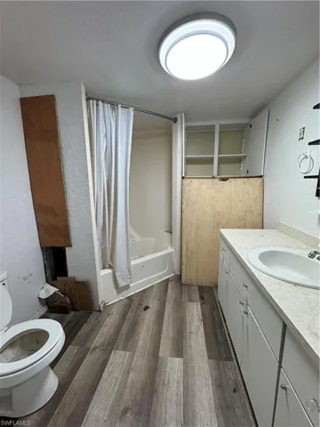 Full bathroom with shower / bath combo with shower curtain, hardwood / wood-style flooring, vanity, and toilet