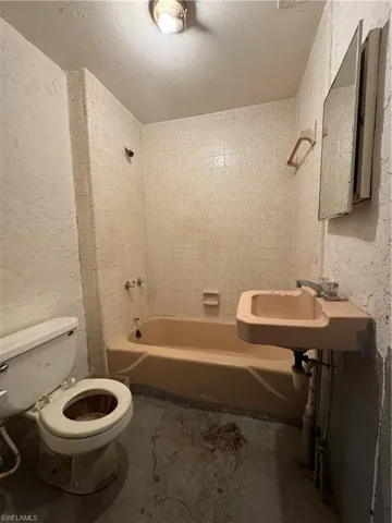 Full bathroom featuring toilet, sink, tub / shower combination, a textured ceiling, and concrete flooring